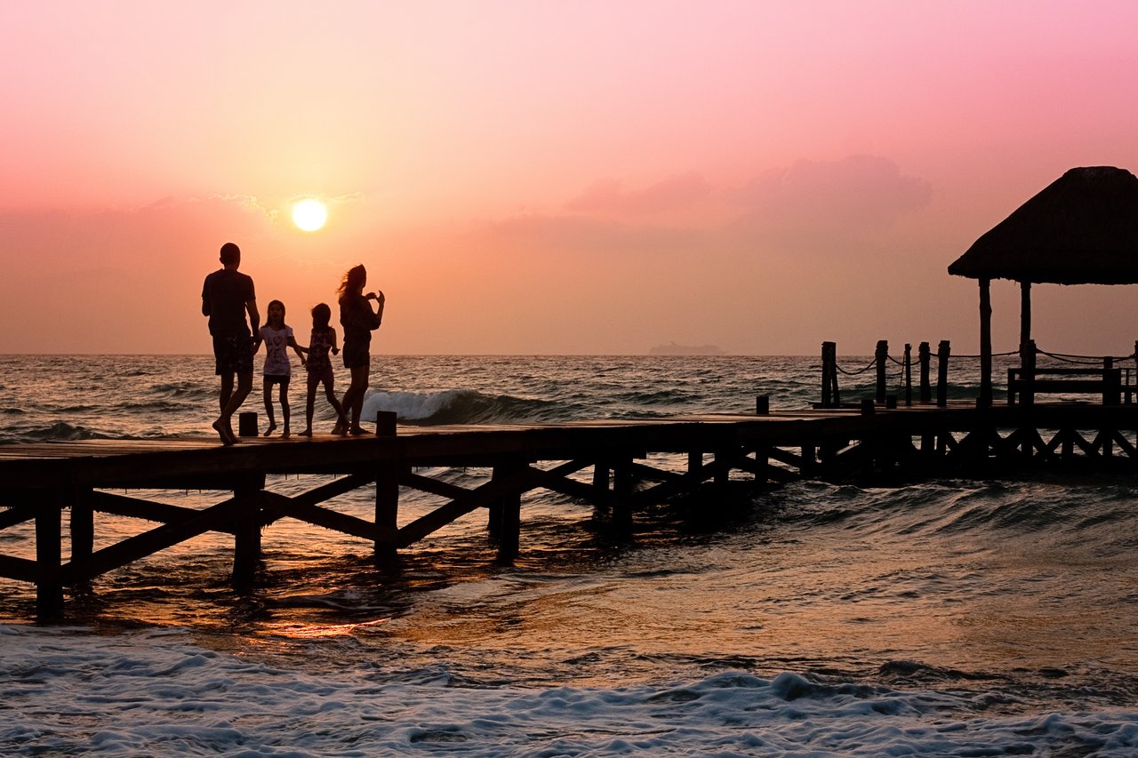 Mastering the First Impression: Your intriguing post title goes here Silhouetted family enjoys a stroll on the beach pier at a vibrant sunset over the ocean waves.