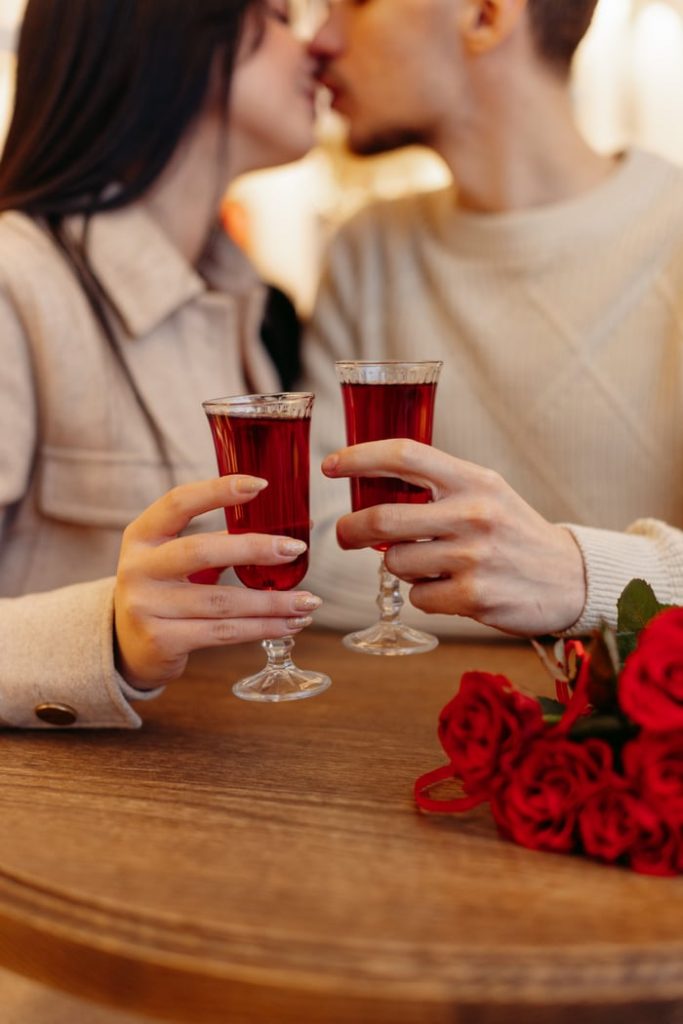 A couple sharing a romantic moment with red drinks and roses, symbolizing love and affection.