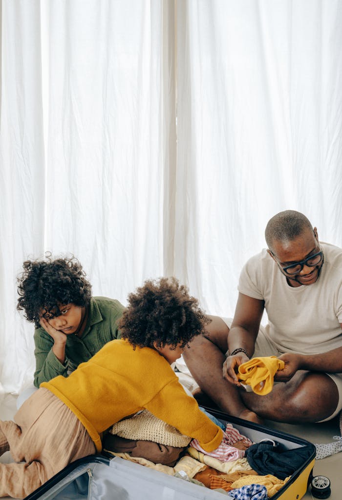 High angle of adorable black girls helping positive father packing suitcase sitting on floor